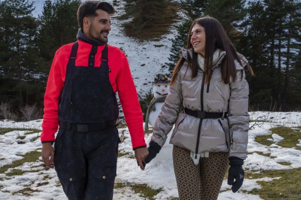 Smiling young couple enjoying a winter walk in the snowy mountains, hand in hand, with a snowman celebrating their romantic relationship and leisure time