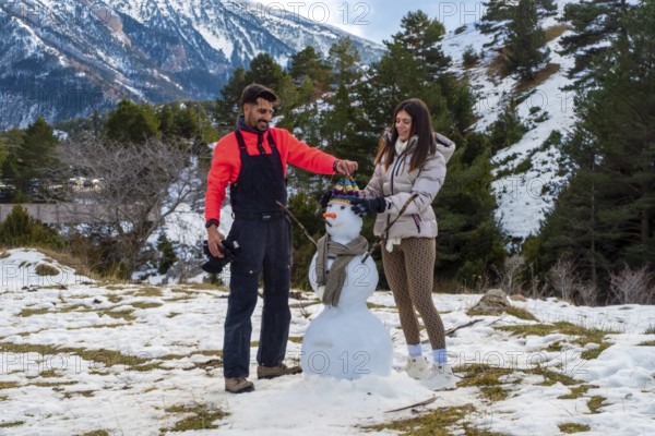 Young couple joyfully building a snowman together in a snowy mountain landscape, celebrating winter outdoor activities and enjoying a shared holiday experience in nature