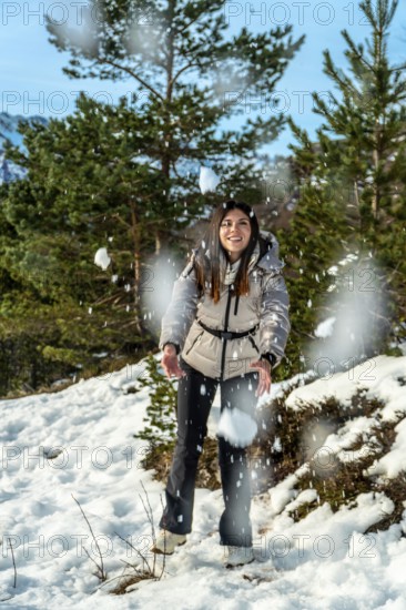 Young woman smiling and catching falling snow in a sunlit pine forest on a mountain winter vacation, playful and joyful outdoors enjoying fresh air and snowy scenery