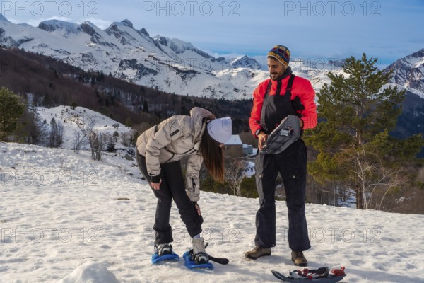 Young couple actively preparing snowshoes on a sunny winter day, ready for a trekking adventure in the snowy mountains, enjoying the clear sky and active lifestyle