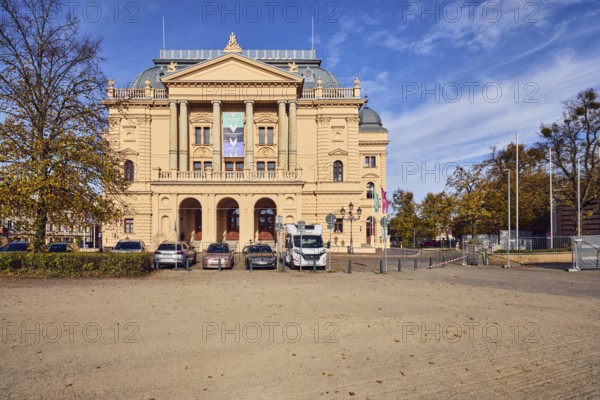 Mecklenburgisches Staatstheater, theatre, historic building, architect Georg Daniel, neo-Renaissance style, flagpoles, parking boxes with cars and motorhomes, barrier bollards, trees, hedge, autumn leaves, blue sky, altocumulus clouds, Alter Garten street, Schwerin, state capital, district-free city, Mecklenburg-Western Pomerania, Germany