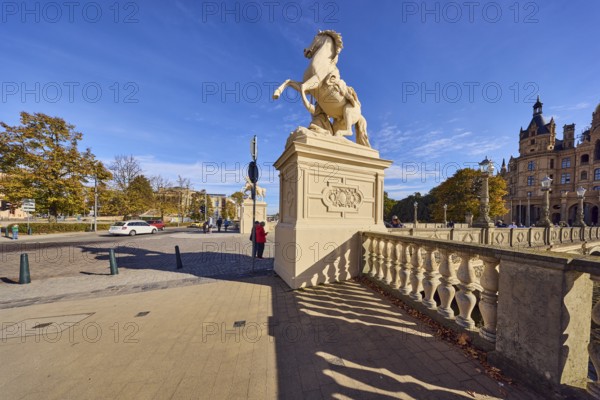 Castle bridge, entrance portal, horse sculpture, car bridge and footbridge, sidewalk, sandstone railing, shade of railing, lantern, general architecture, trees with autumn leaves, car, pedestrian as accessories, blue sky, cumulus clouds, Lennéstraße, Werderstraße and Schlossstraße intersection, Schwerin, state capital, district-free city, Mecklenburg-Western Pomerania, Germany