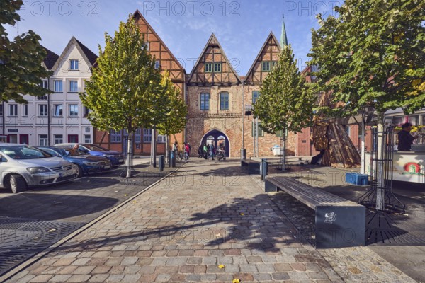 Row of houses, old town, half-timbered building, brick building material, residential building, passage arch, benches, parking lot with cars, trees, autumn leaves, cobblestone walkway, beer car, blue sky, cirrostratus clouds, slaughtermarket, Schwerin, state capital, district-free city, Mecklenburg-Western Pomerania, Germany