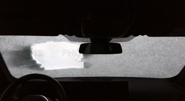 View from a car through a peephole and a windshield partly covered with snow in winter