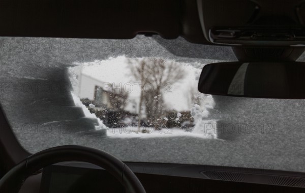 View through a peephole of a partially cleared icy car window with snow showing winter