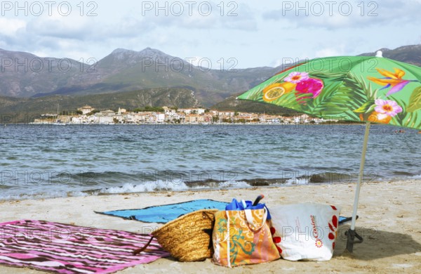 Sunshade and swimwear blurred on the beach or Plage de la Roya, in the back Saint-Florent on the Gulf of Saint-Florent in the Mediterranean, Haute-Corse, Corsica