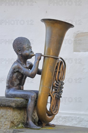 Sculpture boy with tuba by Guido Messer 1991, modern art, bronze sculpture, playing music, tuba, brass instrument, sitting, jack, size comparison, big, small, big cheeks, blowing, half-timbered house, music school, Waldenbuch, Baden-Württemberg, Germany