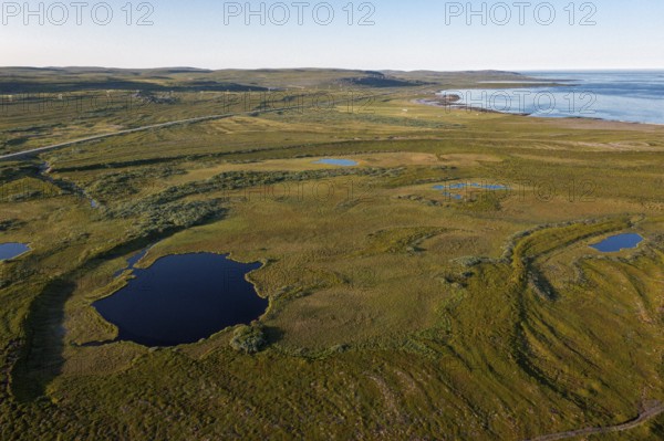 Coastal landscape on Varangerfjord with blue sky, still sea, moors and pebble beach aerial view, Barents Sea, Finnmark, Norway