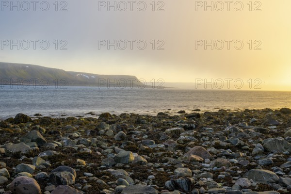 A peaceful beach at sunset with rocks and calm sea under a slightly cloudy sky, Båtsfjord, Finnmark, Norway
