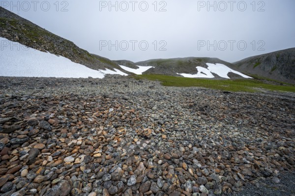 Barren mountain landscape with stones, snow and foggy sky, looks cold and rough, beach walls on Tanafjord, Finnmark, Norway
