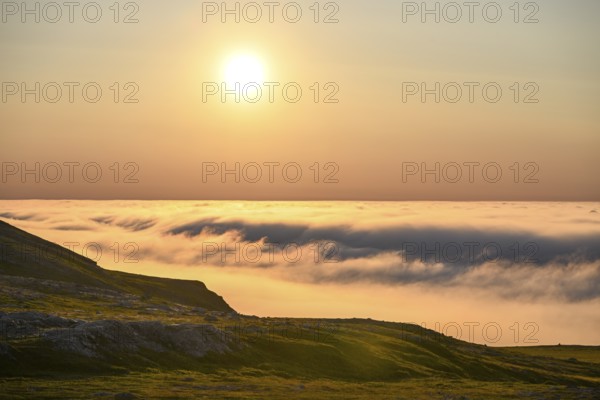 View from Mount Domen. Dense sea fog hangs over the Barents Sea the midnight sun shines in the north in an orange sky, Domen, Vardö, Finnmark, Norway
