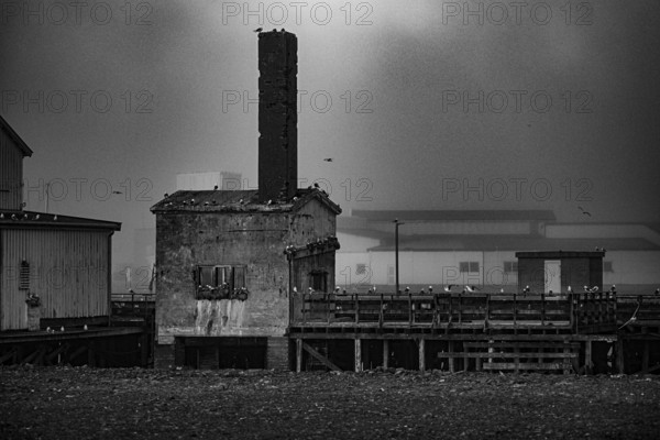 Abandoned industrial building in the old port of Vardö with a chimney in a foggy environment, Vardø, Finnmark, Norway