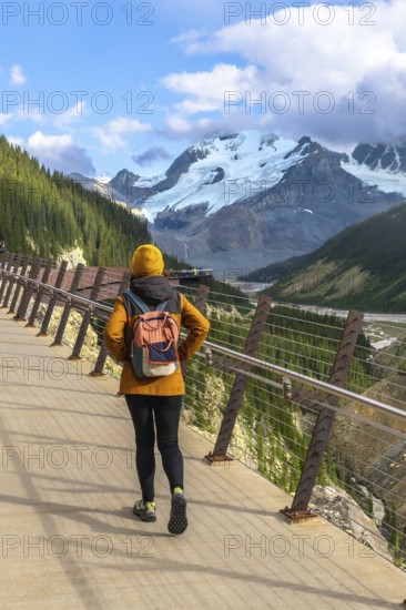 Hiker walking along the glass floored skywalk enjoying the scenic view of the athabasca glacier and the canadian rockies in jasper national park, alberta, canada