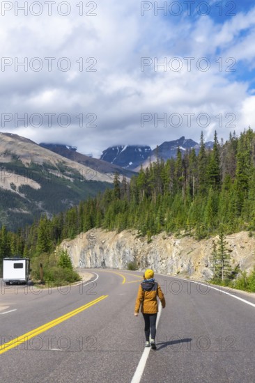 Female tourist walking on the iconic icefields parkway in the canadian rockies, enjoying breathtaking mountain views on a sunny day with a camper van parked on the side of the road