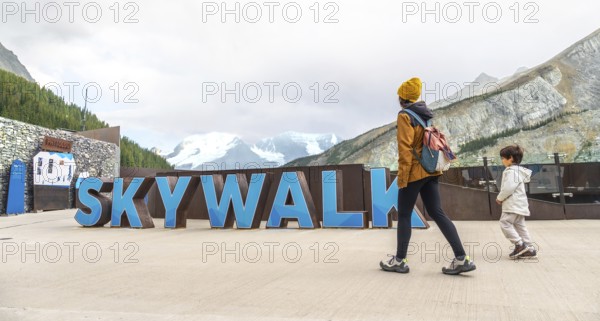 Tourists walking by large skywalk sign with athabasca glacier and mountains in background at columbia icefield in jasper national park, alberta, canada