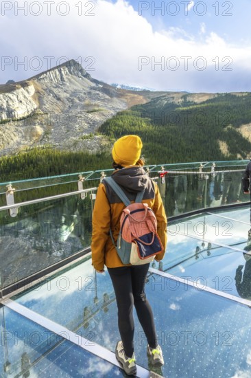 Tourist wearing yellow hat and backpack standing on the glass platform of the glacier skywalk enjoying breathtaking view of athabasca glacier. Canadian rockies. Jasper national park. Alberta. Canada