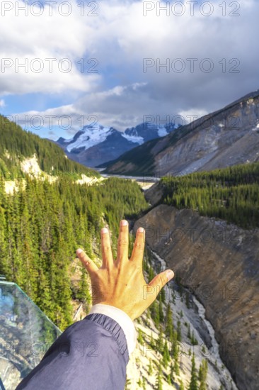 Tourist extending a hand towards the breathtaking valley view from the glass platform of the glacier skywalk, highlighting the natural beauty of the canadian rockies