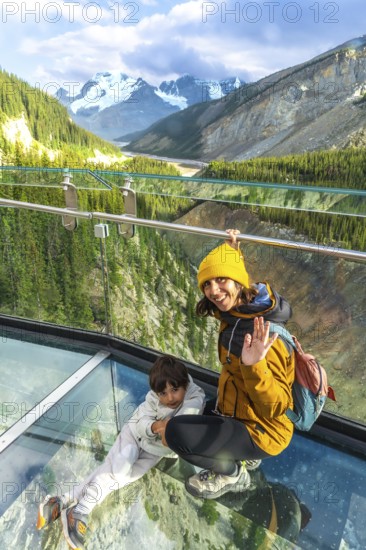 Mother and child waving from the glass platform of the glacier skywalk, enjoying the stunning panorama of the sunwapta valley and the canadian rockies in jasper national park, alberta, canada
