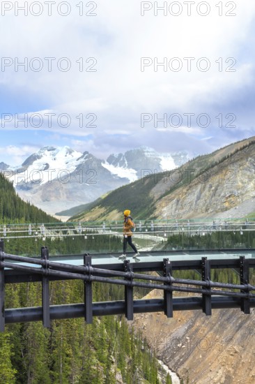Tourist walking on a glass skywalk, taking in stunning views of the athabasca glacier and the majestic mountains in jasper national park, alberta
