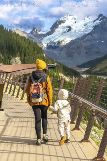 Mother and child walking on the glass floored skywalk, taking in stunning views of athabasca glacier and the majestic mountains of jasper national park, alberta