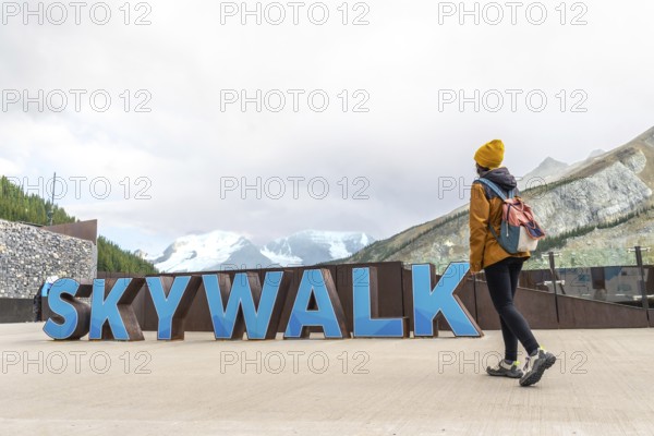 Female tourist walking near the skywalk sign with the athabasca glacier and mountains in the background at the columbia icefield in jasper national park, alberta, canada