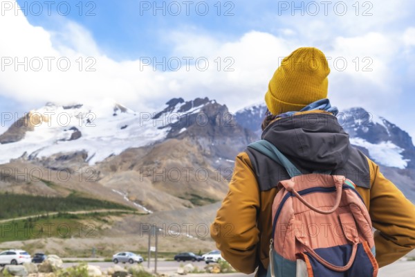 Hiker wearing a yellow beanie and carrying a backpack enjoying the breathtaking view of the athabasca glacier in jasper national park. Alberta. Canada. A popular tourist destination for nature lovers