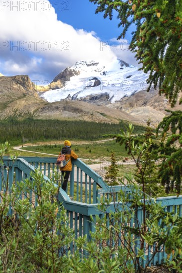 Tourist with backpack standing on wooden turquoise viewpoint is admiring stunning view of athabasca glacier in jasper national park, alberta, canada