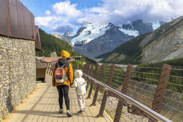 Mother and child walking on the glacier skywalk, enjoying the breathtaking view of the athabasca glacier and the canadian rockies in jasper national park, alberta, canada, on a sunny day