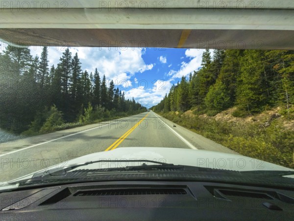 White car driving on a scenic highway through a coniferous forest in the canadian rockies on a sunny summer day, offering a breathtaking view of the natural landscape