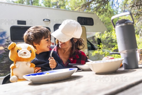Mother and son are sitting at a picnic table, enjoying breakfast outside their campervan in banff national park, surrounded by the beauty of the canadian rockies