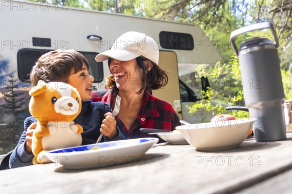 Mother and son laughing together while enjoying breakfast at a picnic table outside their camper van in banff national park, capturing a joyful moment of family bonding