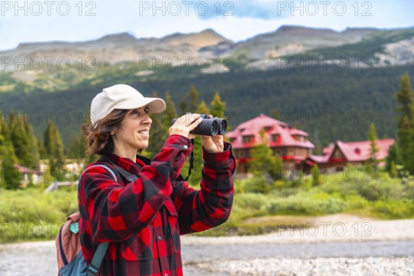 Female tourist using binoculars enjoying the landscape at bow lake with the iconic num ti jah lodge in the background, banff national park, canadian rockies, alberta, canada