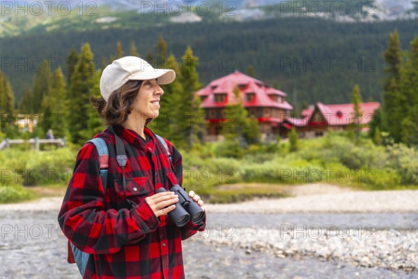 Female tourist holding binoculars enjoying the landscape of bow lake with the red roof of num ti jah lodge in the background, banff national park, alberta, canada