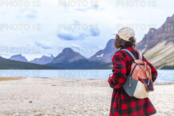 Female tourist with a backpack admiring the breathtaking turquoise waters of bow lake and the majestic mountains in banff national park, alberta, canada