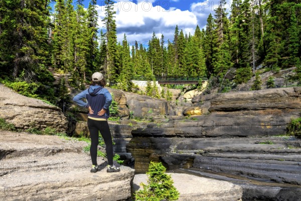 Female hiker standing on a rock formation admiring the layered rock formations of mistaya canyon and bridge in banff national park, canadian rockies, alberta, canada, during a sunny summer day