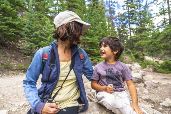 Mother and son taking a break during a hike in mistaya canyon, banff national park, enjoying a joyful moment amidst lush pine trees and rocky paths