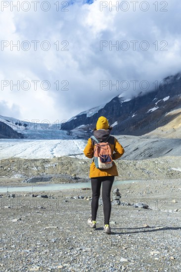 Hiker walking on the rocky terrain towards the athabasca glacier in jasper national park, alberta, with cloudy sky in background, enjoying the stunning views of the canadian rockies