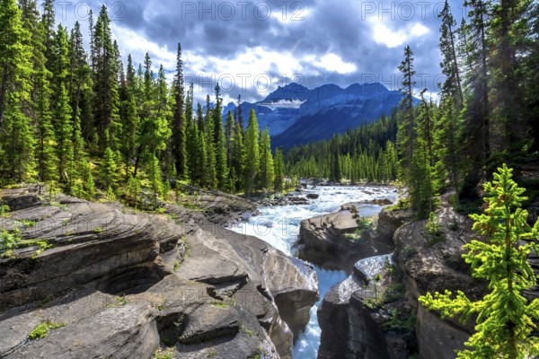 Mistaya river water flows through mistaya canyon in banff national park, surrounded by lush evergreen forest and rocky mountains on a beautiful cloudy day in the canadian rockies, alberta, canada