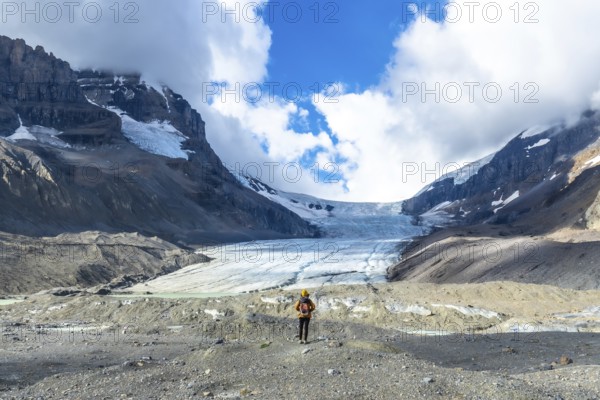 Hiker standing in front of the impressive athabasca glacier in jasper national park, canadian rockies, alberta, under a cloudy sky, admiring the immensity of nature