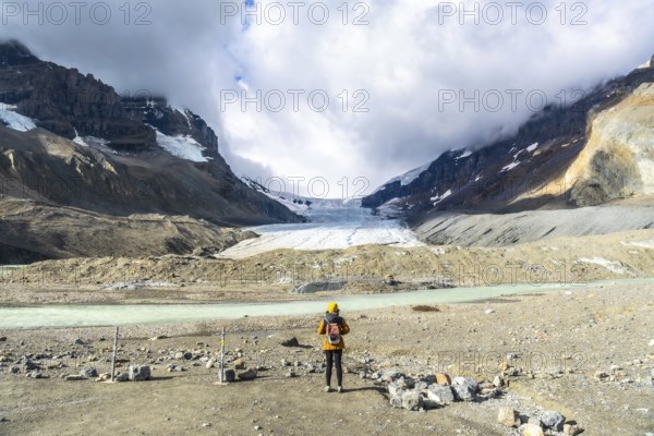 Majestic view of the athabasca glacier in jasper national park, alberta, canada, with a tourist contemplating the impressive ice formation and surrounding mountains on a cloudy day