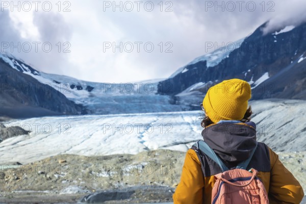 Female hiker in a yellow beanie and backpack enjoying breathtaking views of athabasca glacier in jasper national park, highlighting the region's natural beauty