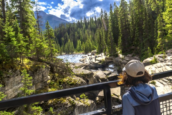 Female tourist admiring the impressive mistaya canyon with its rock formations, lush forest, and powerful river in banff national park, canadian rockies, alberta, canada, during a bright summer day