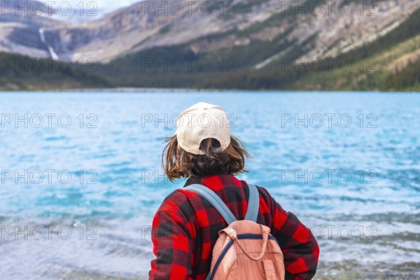Young hiker with backpack and cap enjoying the breathtaking view of bow lake and surrounding mountains in banff national park, a stunning natural wonder in the canadian rockies