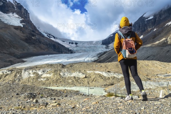 Female tourist with backpack admiring the breathtaking view of athabasca glacier in jasper national park, canadian rockies, alberta, showcasing the beauty of nature and global warming effects