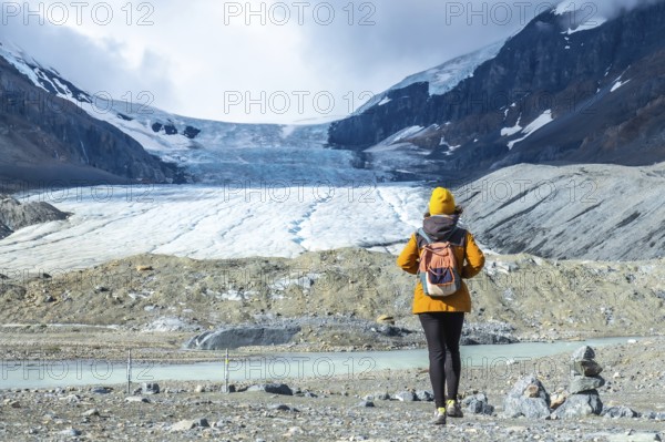 Female tourist with backpack walking towards the athabasca glacier in jasper national park, alberta, canada, admiring the breathtaking view of the canadian rockies and a turquoise glacial lake