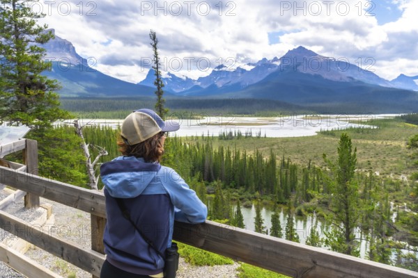 Tourist wearing a baseball cap leans on a wooden fence, admiring the stunning panorama of the north saskatchewan river winding through the majestic canadian rockies in banff national park