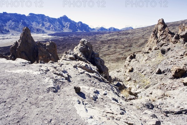 Rough volcanic landscape with rocky mountains in the background under clear sky, Pico del Teide National Park, La Orotava Tenerife