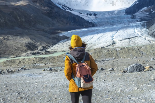 Female hiker in a yellow jacket and backpack admiring the majestic athabasca glacier in jasper national park, alberta, highlighting the impacts of global warming