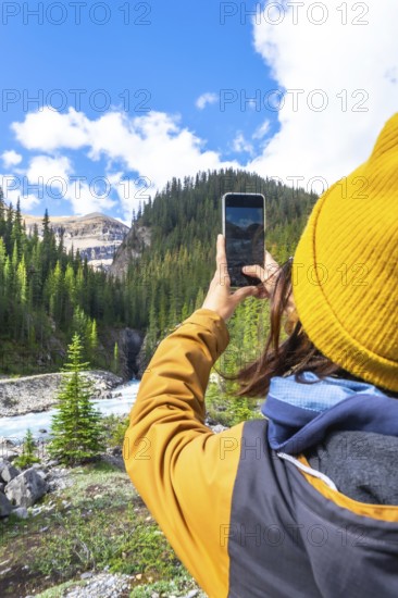 Female hiker capturing scenic waterfall photos with a smartphone along ci fuentes path on the icefields parkway in the canadian rockies, enjoying breathtaking views