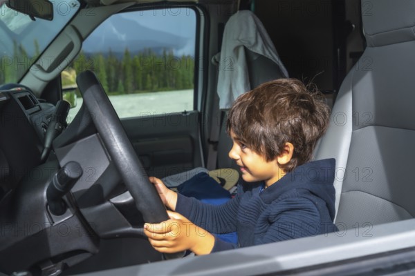 Happy child pretending to drive a vehicle while enjoying a scenic road trip through the mountains of the canadian rockies, creating a heartwarming moment of childhood adventure and family travel